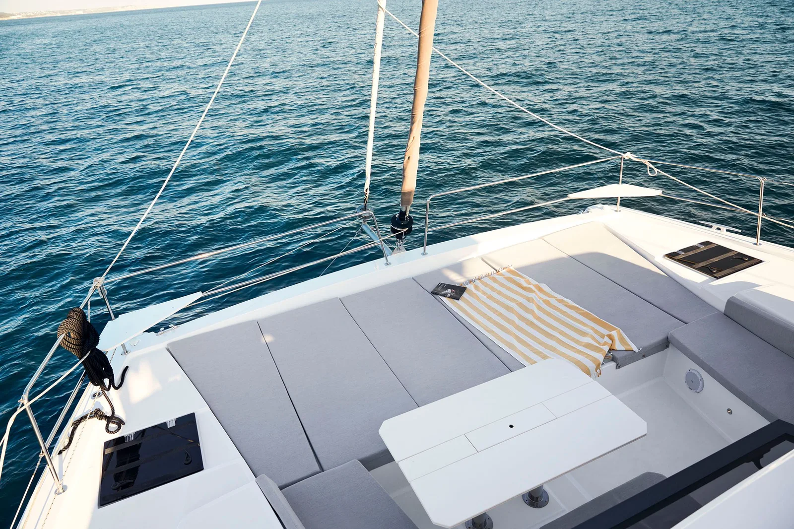 Bali 4.6 forward deck with wide cushioned sunpads and a recessed table beside the sea