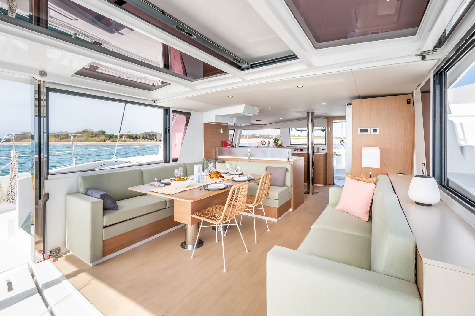 Bali 4.6 saloon with a dining table, sofas on both sides and the aft door lifted open